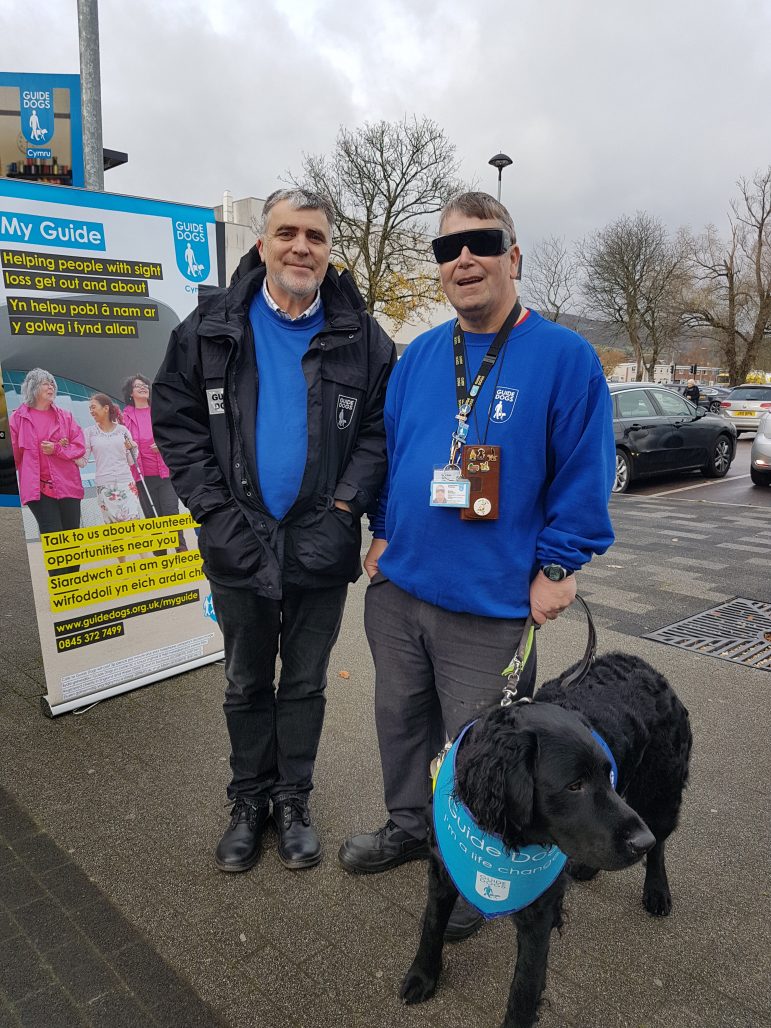A visually impaired man with his guide dog and a volunteer from Blind Dogs Cymru