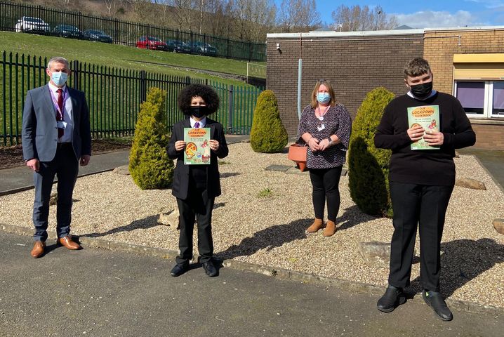 Two pupils holding the cook book with two staff members