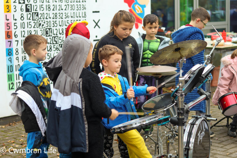 A boy plays the drums with children watching him