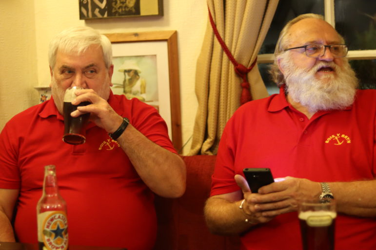 a man drinking beer next to man on phone
