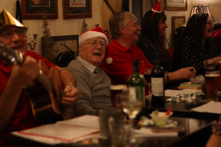 a man in santa hat singing next to man with guitar