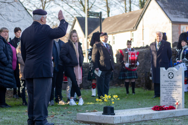 A former serviceman salutes in front of a grave