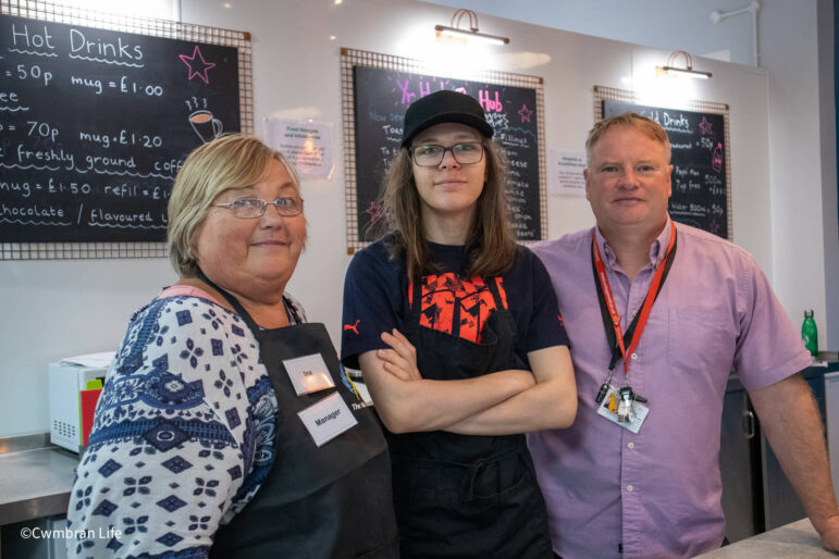 a woman and two men by a cafe menu board