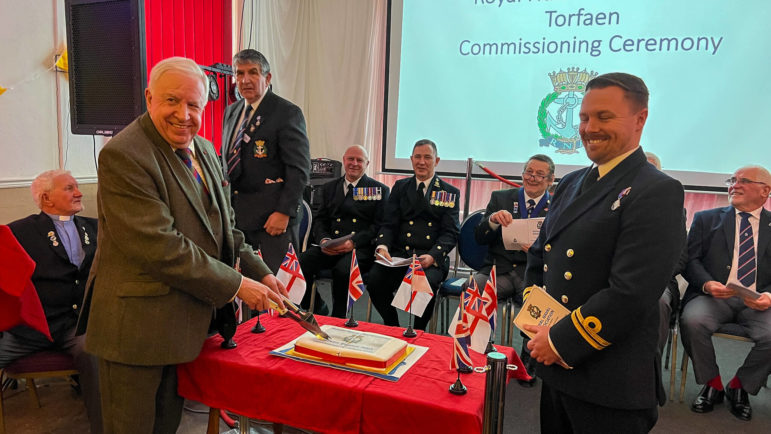 a man cuts a cake watched by other people