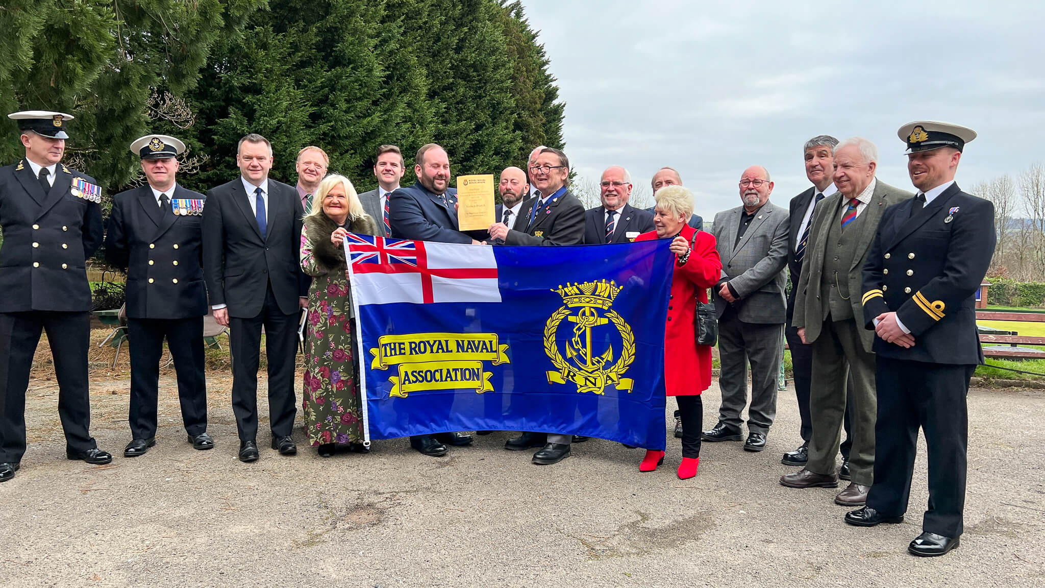 group of people hold the royal naval association flag