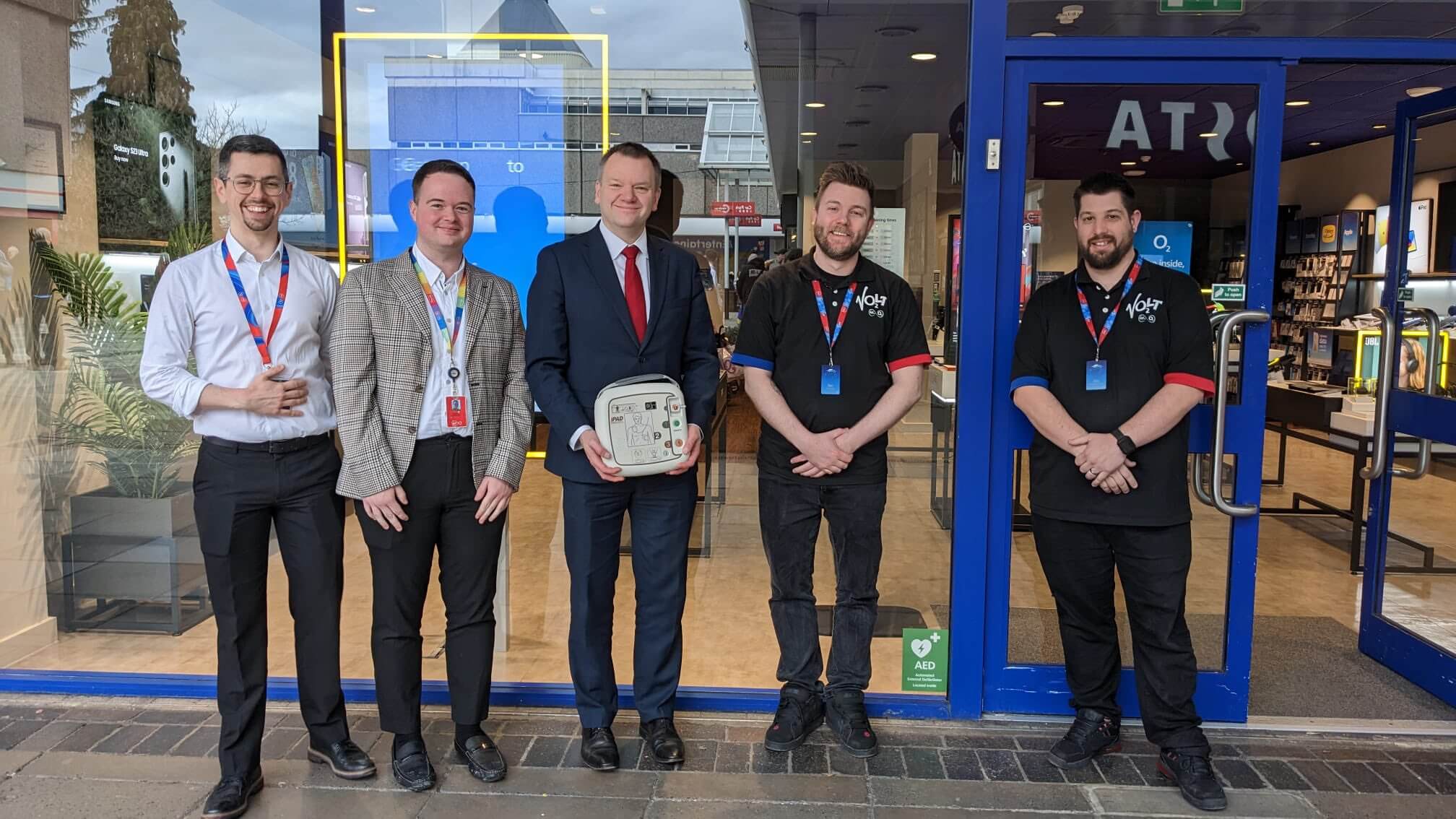 a group of people outside a shop holding a defibrilator