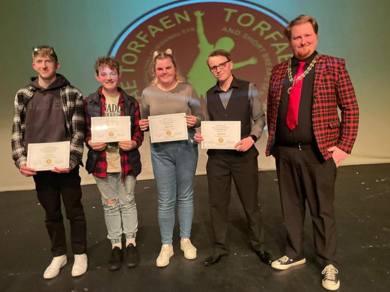 four young people hold certificates stood next to a councillor
