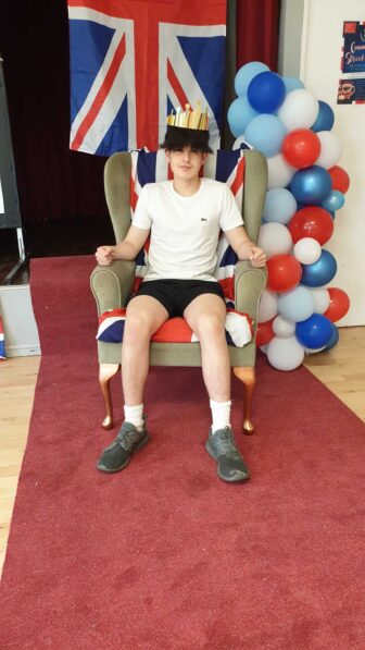 a teenage boy sat in a 'throne' with a union jack flag