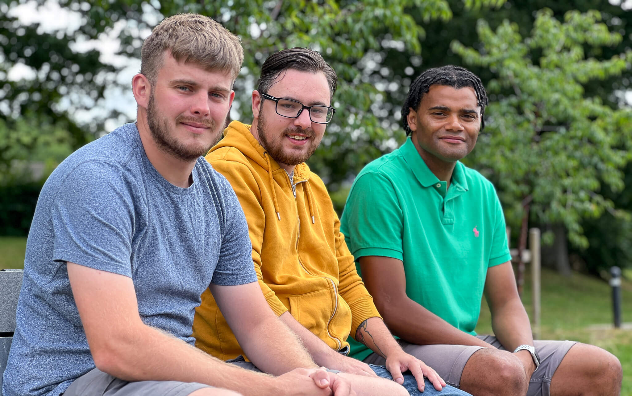 three men sat on a bench smiling at camera