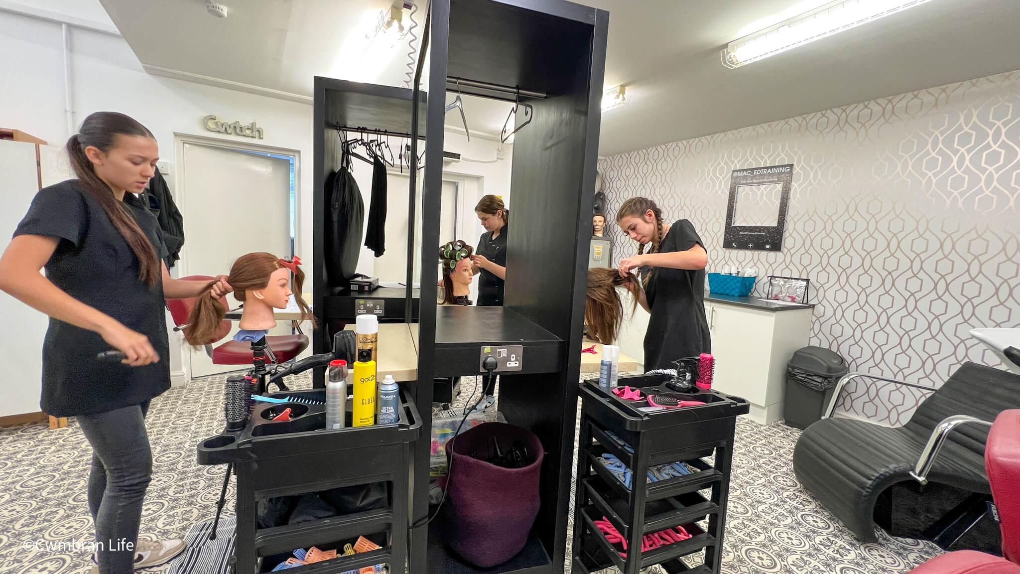 three hairdressing students cut hair on plastic models