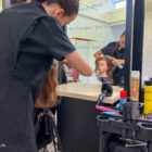a hairdressing student sprays hairspray on a plastic model