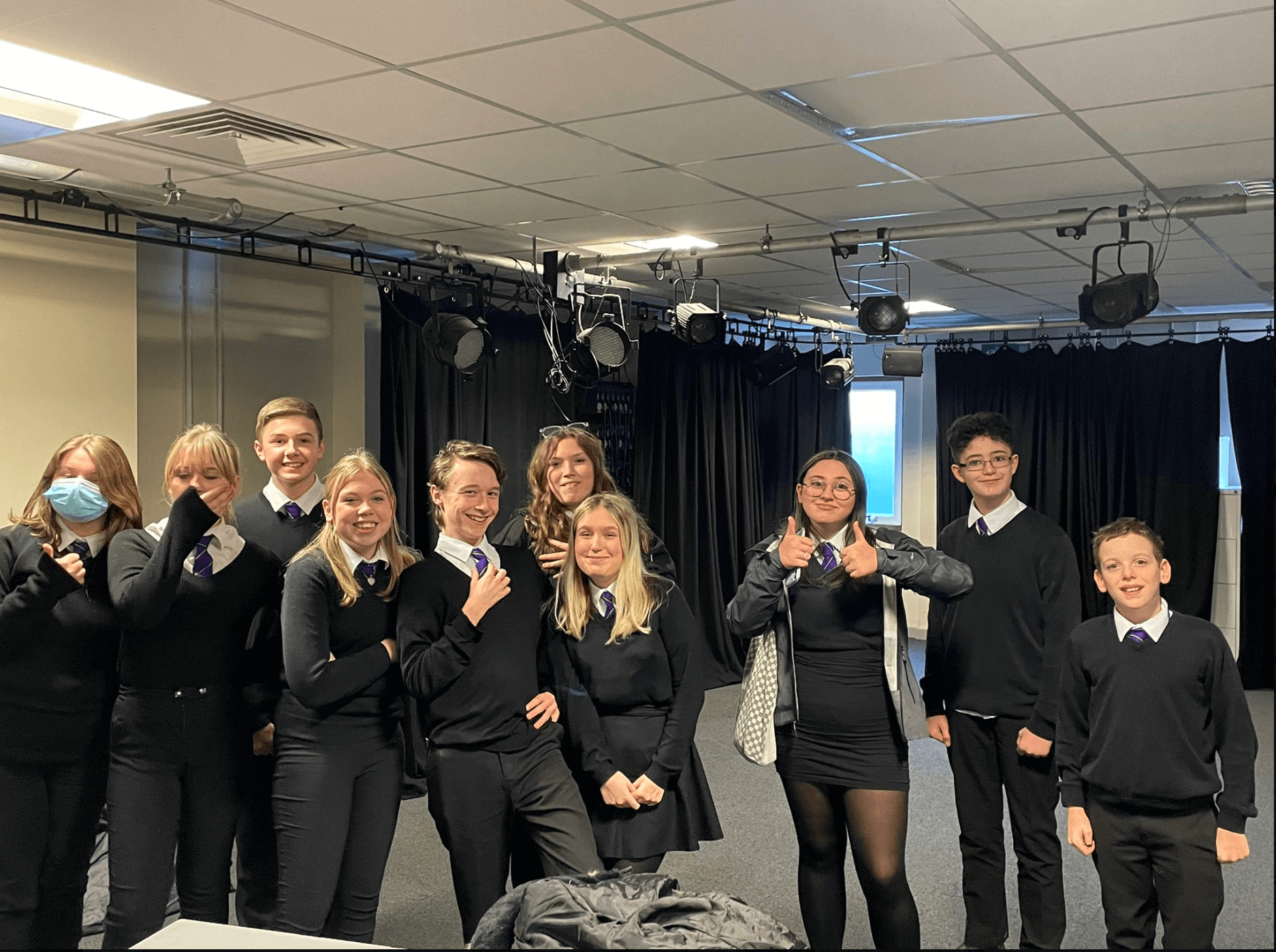 pupils in a school drama group stood in a row smiling at camera
