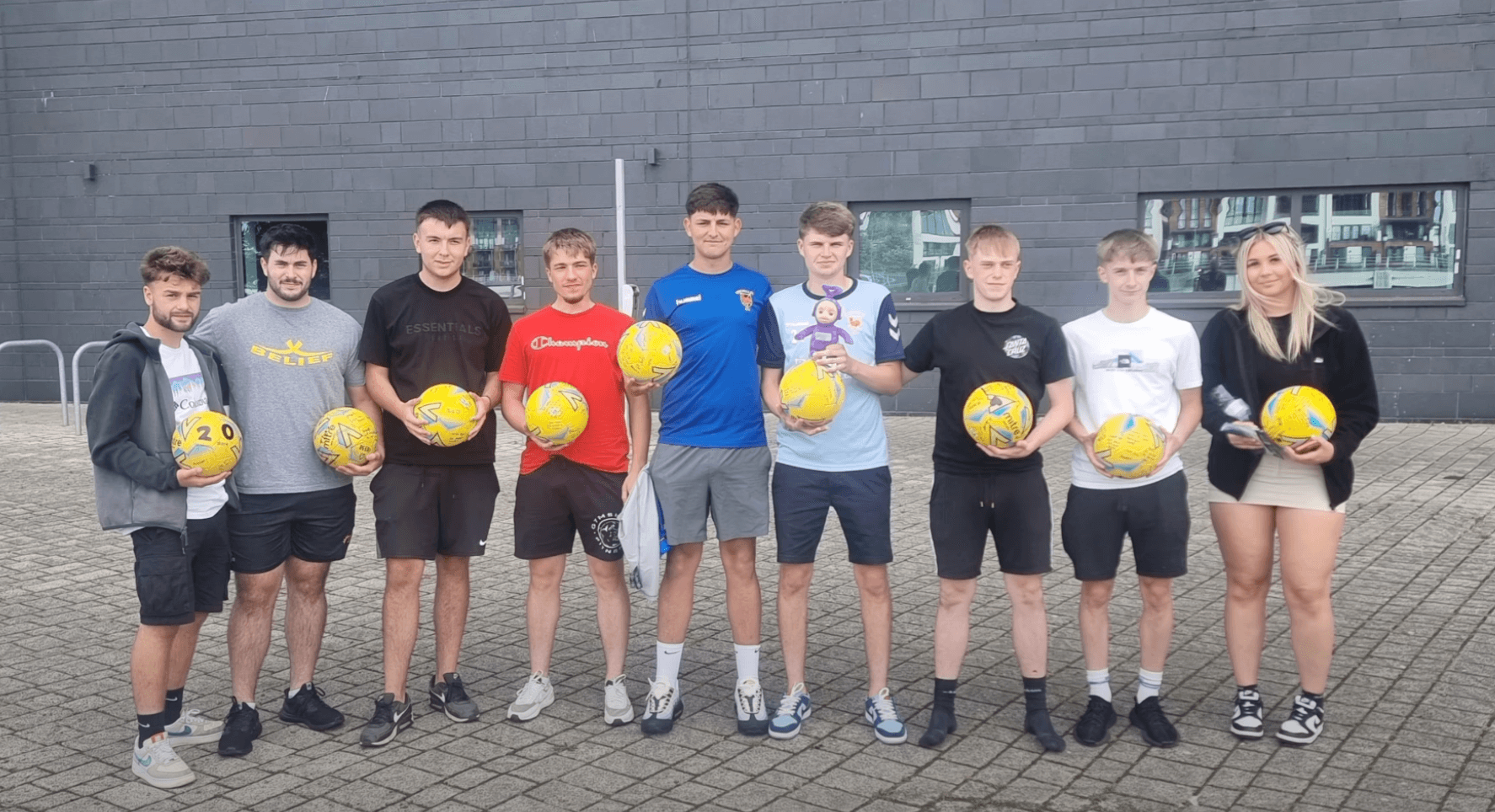 a group of teenagers in a row, each of them holding a football