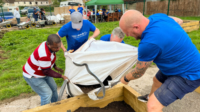 four men empty a bag of soil into a raised bed