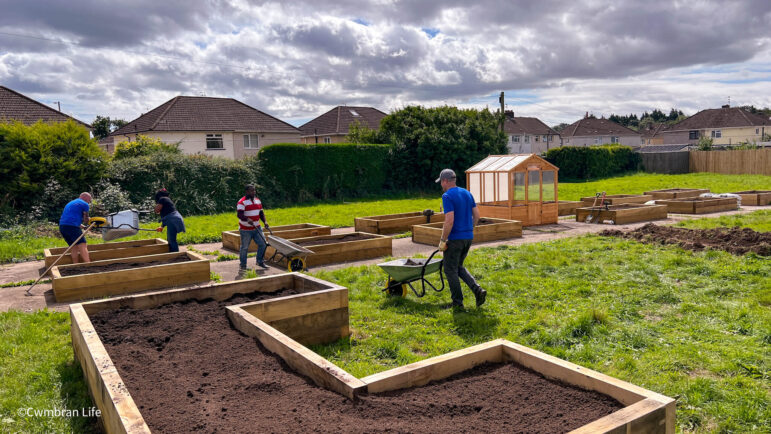 a allotment with over ten raised bed and people filling them up with soil