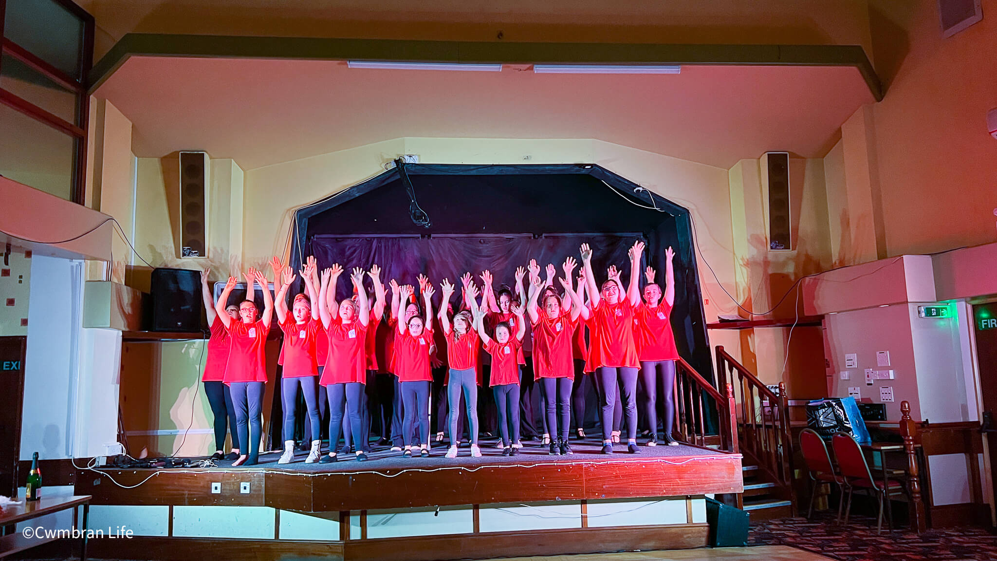 group of children and adults on a stage with arms in air