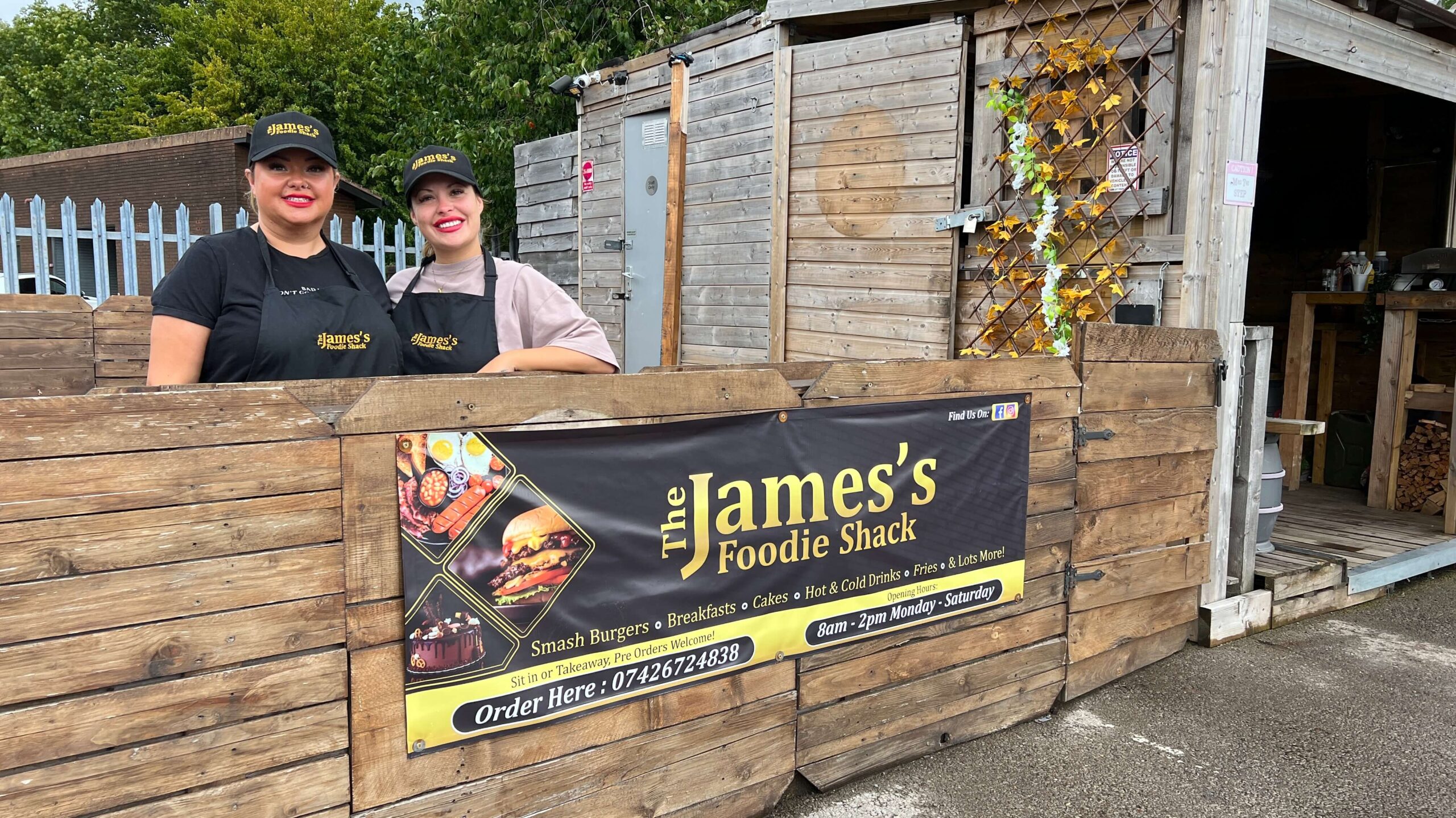 two women leaning over fence by a burger business