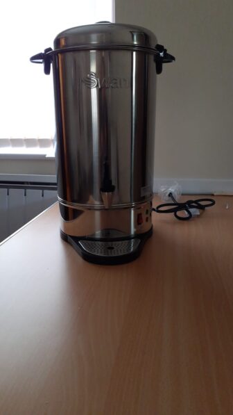 a hot water urn- a large steel container for hot water on a table