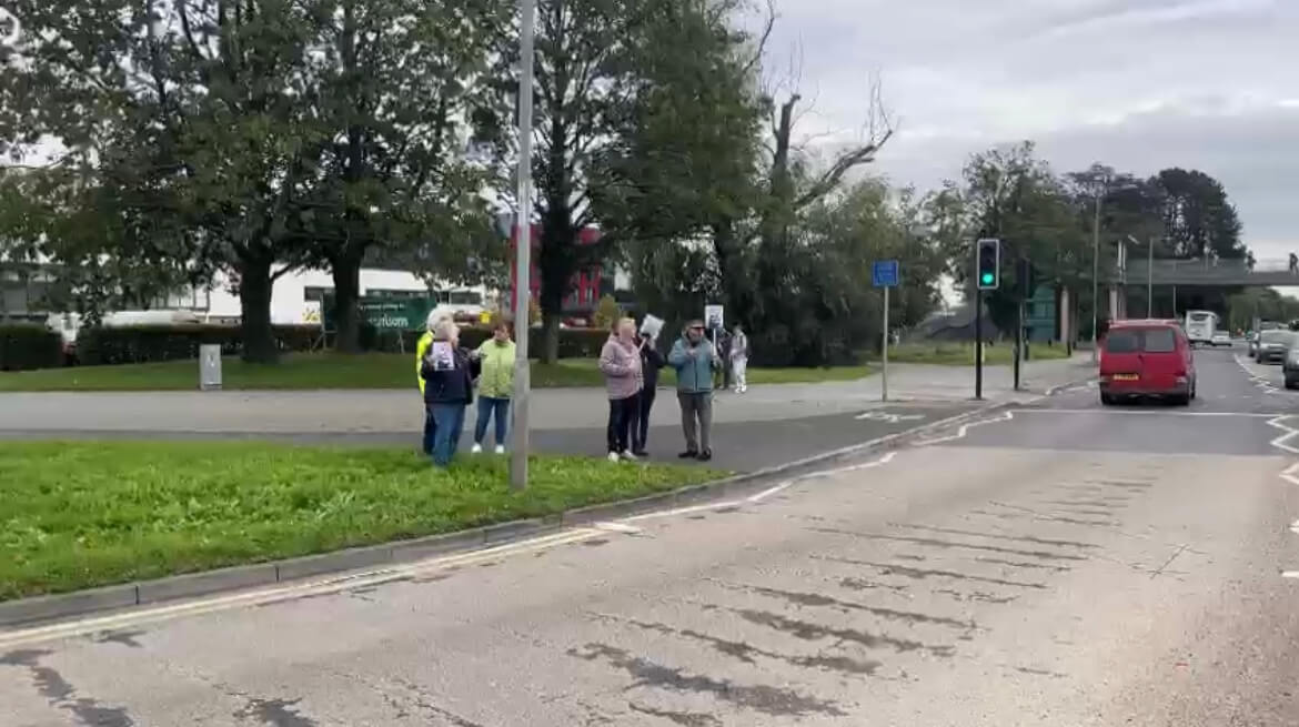 group of protestors hold signs by a road