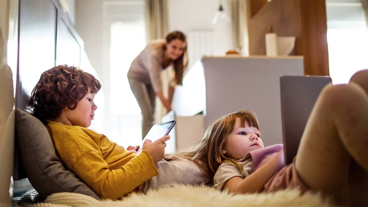 children lying on floor holding a phone and laptop