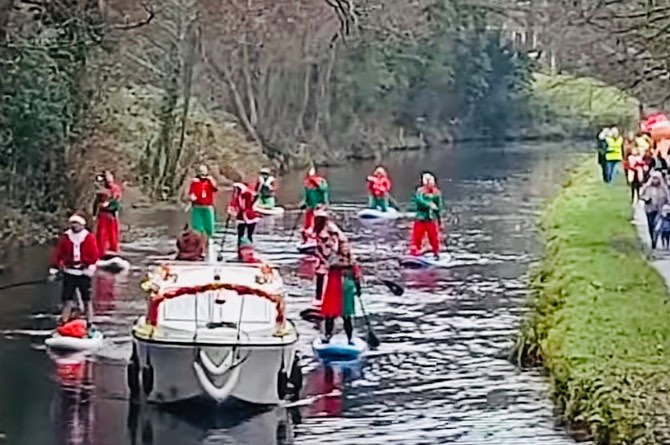 a boat with Santa on it followed by people on paddleboards dressed as elves