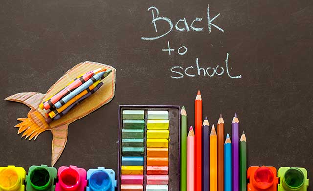 pencils and crayons by a blackboard that says 'back to school'
