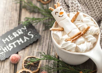 a cup of white hot chocolate next to a merry christmas sign