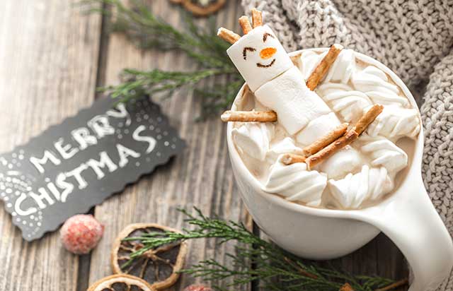 a cup of white hot chocolate next to a merry christmas sign