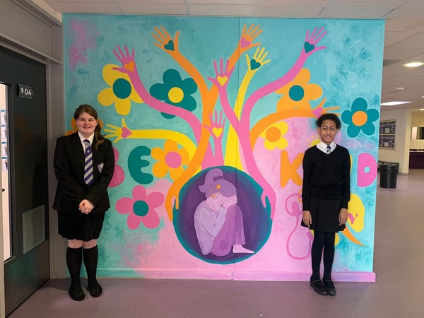 two pupils stood by a mural