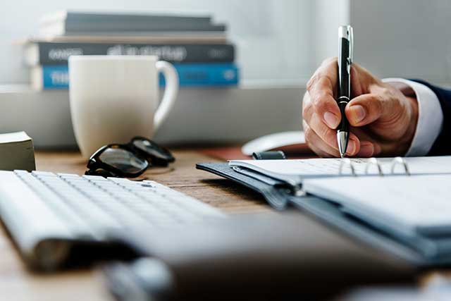 man's hand writing next to keyboard