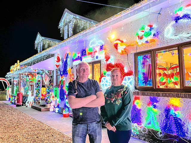 a man and woman outside a house covered in christmas lights