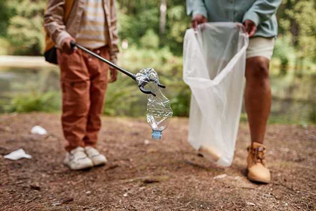 a girl puts litter in a bag held by an adult