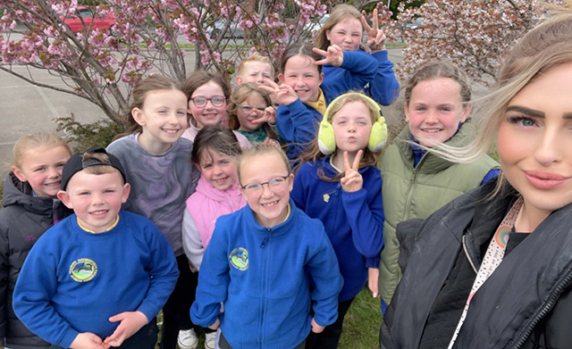 children stood by a blossom tree with their teacher