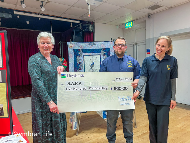 three people hold a large cheque