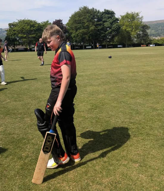 a teenage boy on a cricket pitch with a bat