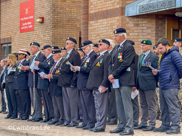 Veterans at the VE day service in Cwmbran stand in two lines- most wearing medals and berets