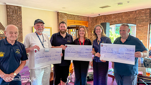 six people line up and hold three large cheques