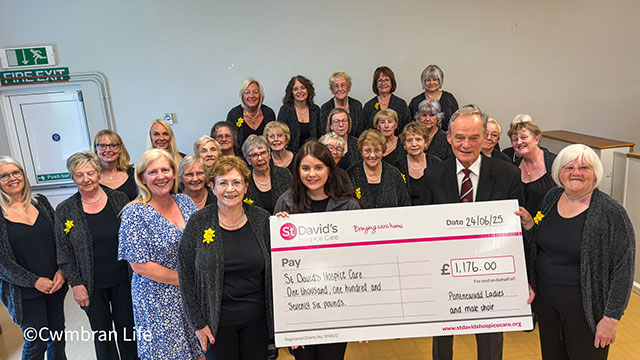 a large group of women and two men- a few are holding a large charity cheque