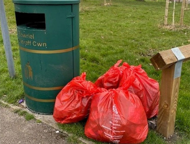 red bin bags full of rubbish by a bin