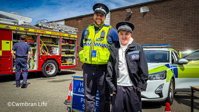 a police officer by a car with a young teenage boy in a police hat
