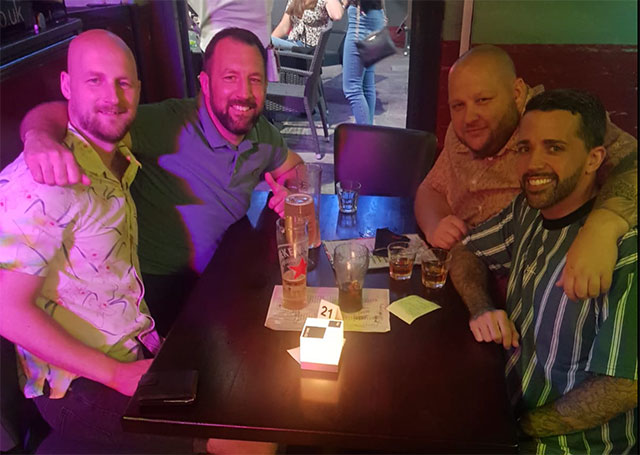 four men at a table in a restaurant with arms around each other