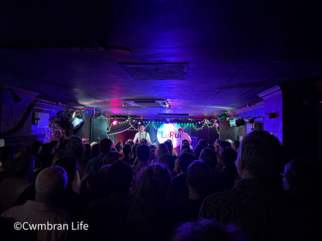 two men sing and play guitar at front of a gig
