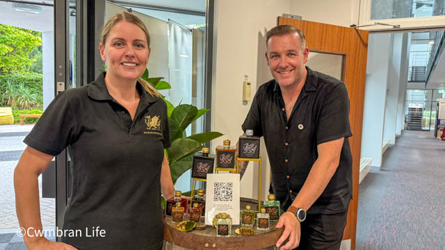 a man and woman stood by some spirit bottles in an officer