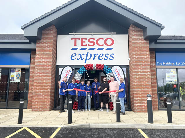 a group of people at a ribbon cutting event outside a Tesco express