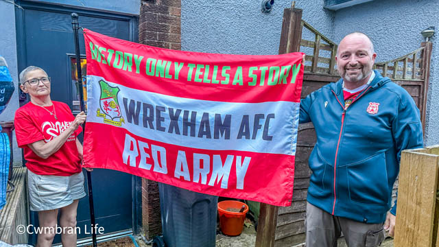 a man and woman hold a red flag for Wrexham AFC