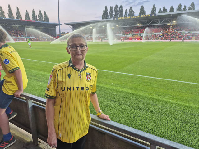 a woman in a yellow football shirt by a pitch