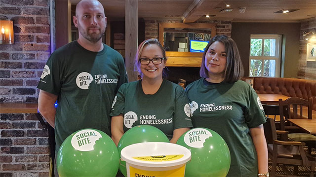 three people stood behind a money collection bucket and green balloons