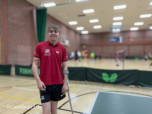 a man in red top in a sports hall by a table tennis table