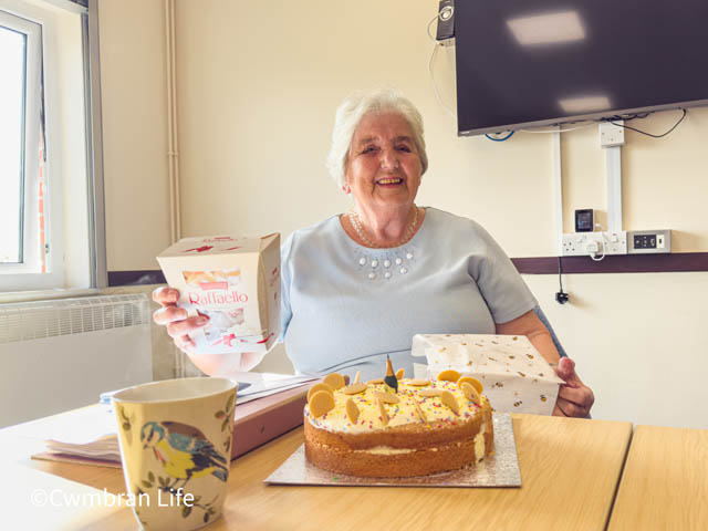 a woman sat by her birthday cake at a table