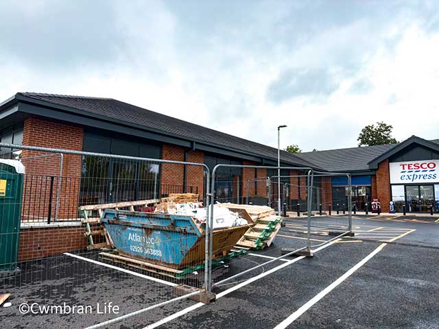 a skip in a car park in front of some shop units
